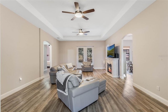 living room featuring dark wood-type flooring, ceiling fan, and a tray ceiling