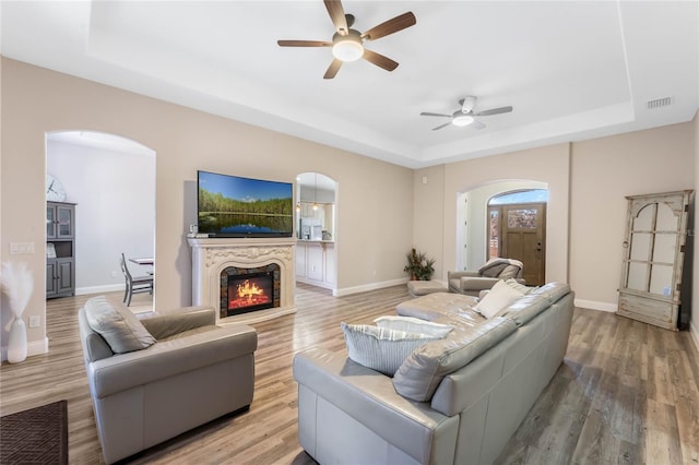 living room featuring a raised ceiling, ceiling fan, and light wood-type flooring