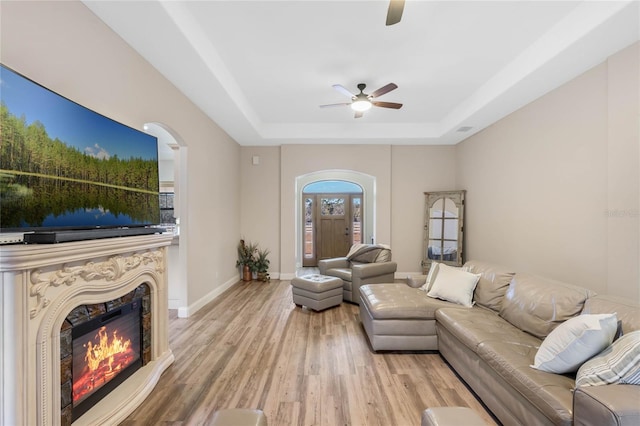 living room featuring ceiling fan, a high end fireplace, light wood-type flooring, and a tray ceiling