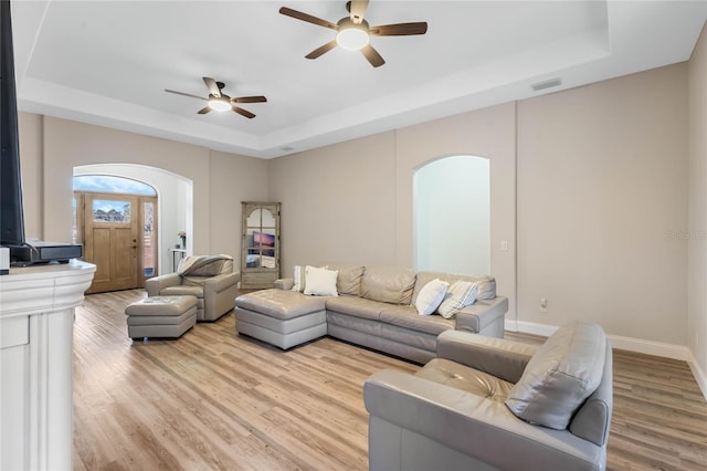 living room featuring light hardwood / wood-style flooring, ceiling fan, and a tray ceiling