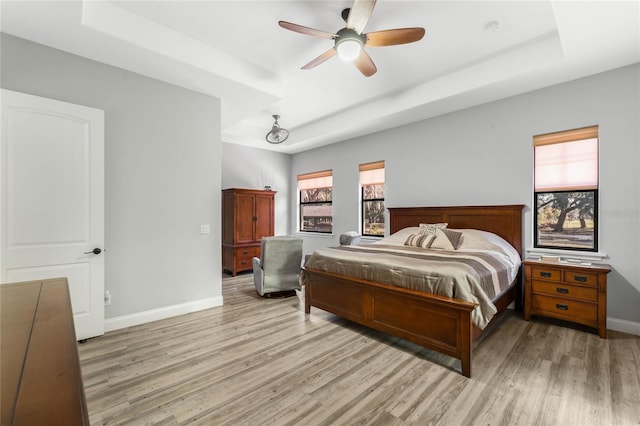 bedroom with light wood-type flooring, ceiling fan, and a tray ceiling