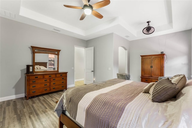 bedroom with ceiling fan, a tray ceiling, and light hardwood / wood-style floors