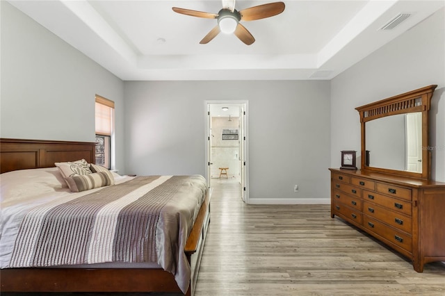 bedroom with a tray ceiling, light wood-type flooring, ceiling fan, and ensuite bathroom