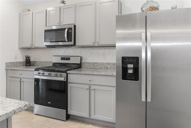 kitchen featuring gray cabinetry, light stone counters, tasteful backsplash, light tile patterned floors, and appliances with stainless steel finishes