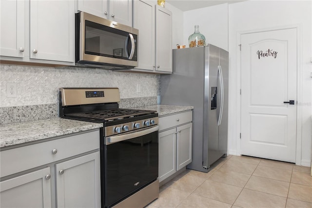 kitchen featuring gray cabinets, appliances with stainless steel finishes, backsplash, light stone counters, and light tile patterned flooring