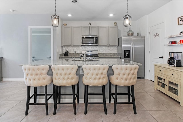 kitchen featuring pendant lighting, appliances with stainless steel finishes, a center island with sink, and gray cabinetry