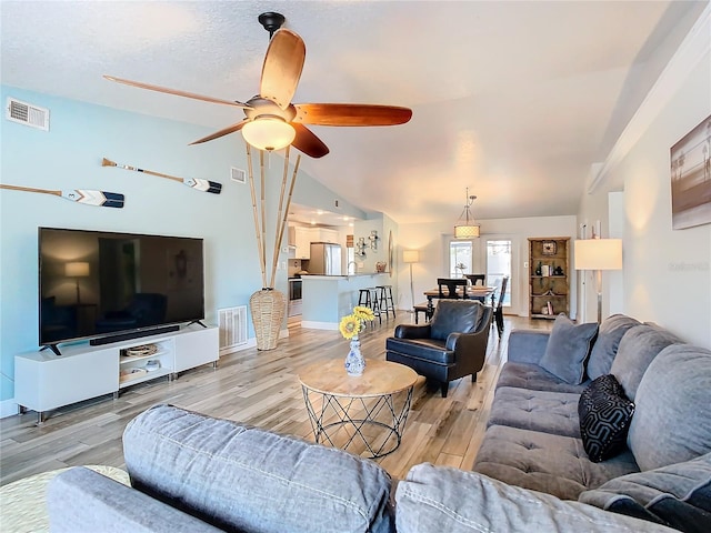 living room featuring ceiling fan, lofted ceiling, a textured ceiling, and light wood-type flooring