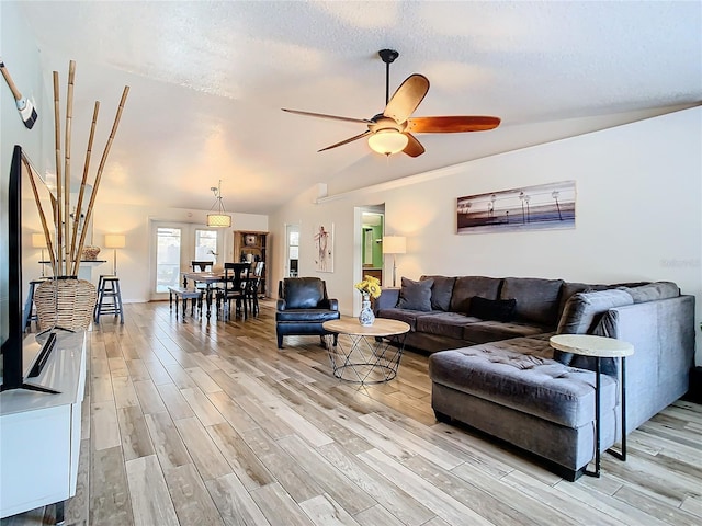 living room featuring light hardwood / wood-style flooring, ceiling fan, vaulted ceiling, and a textured ceiling