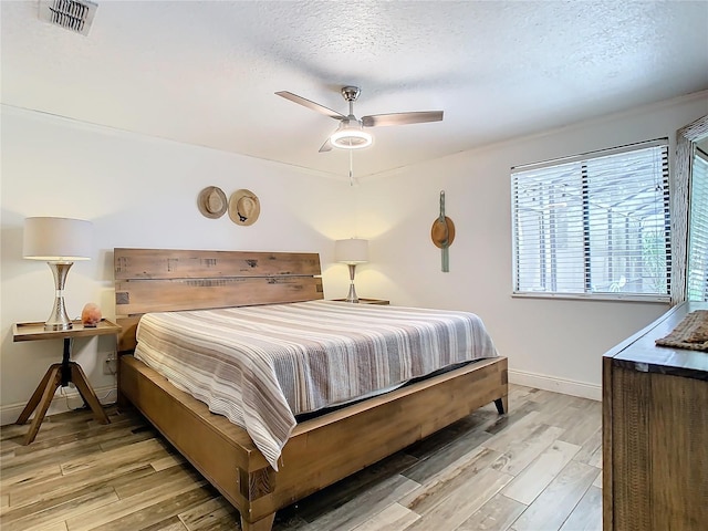 bedroom with a textured ceiling, ceiling fan, and light hardwood / wood-style flooring