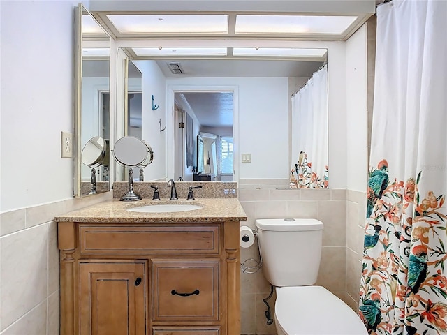 bathroom with vanity, toilet, and tile walls