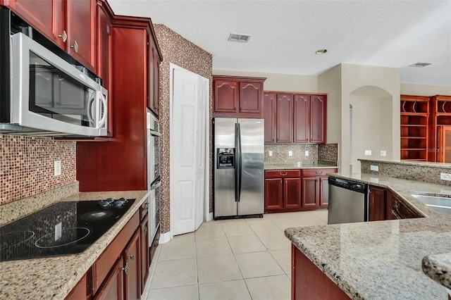 kitchen featuring stainless steel appliances, tasteful backsplash, light tile patterned flooring, a textured ceiling, and light stone counters