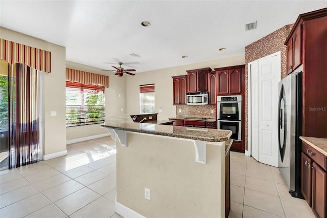 kitchen featuring light tile patterned flooring, stainless steel appliances, and dark stone counters