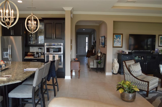 kitchen featuring dark brown cabinetry, appliances with stainless steel finishes, light tile patterned floors, light stone counters, and a chandelier