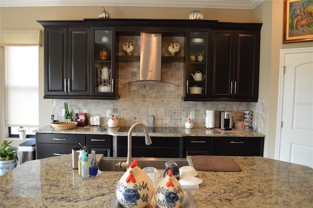 kitchen featuring light stone countertops, crown molding, wall chimney exhaust hood, and tasteful backsplash