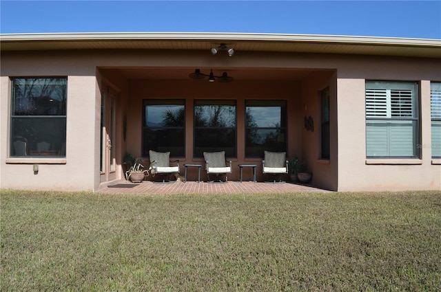 view of exterior entry with ceiling fan, a patio area, and a lawn