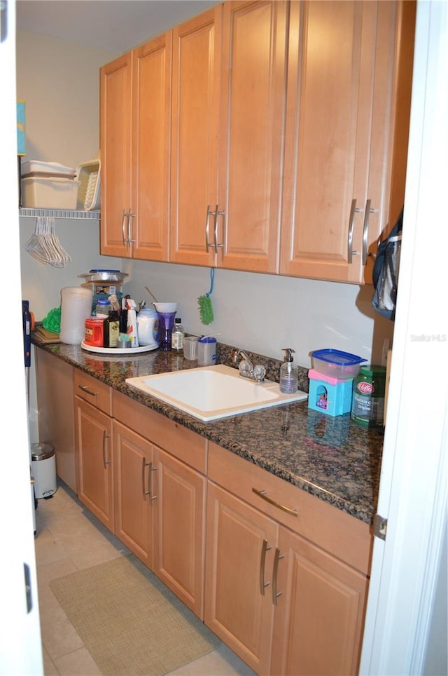 kitchen with light tile patterned floors, sink, and dark stone countertops