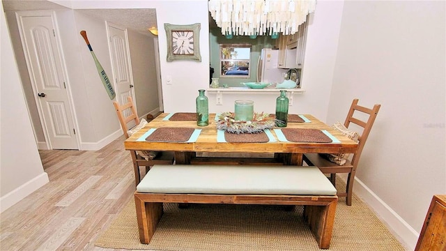 dining space featuring a textured ceiling, light wood-type flooring, and an inviting chandelier