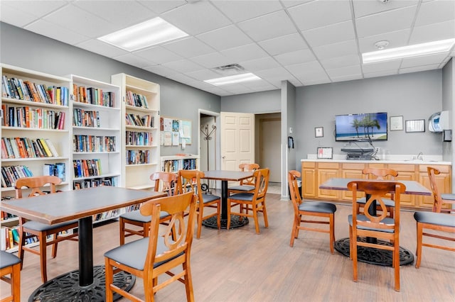 dining room featuring light wood-type flooring, a drop ceiling, and sink