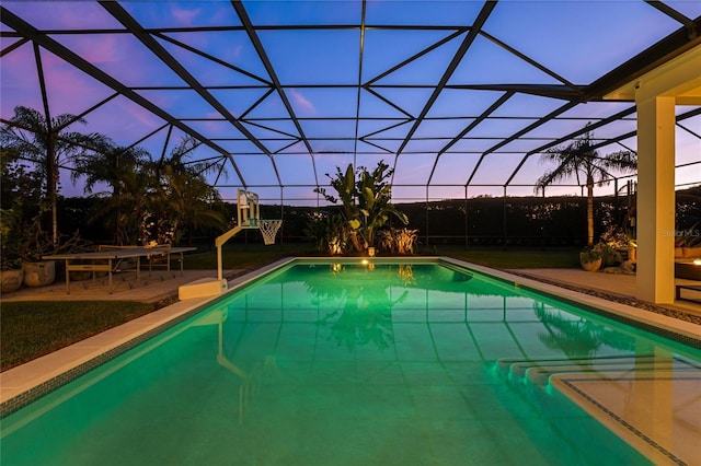 pool at dusk with a patio, glass enclosure, and a playground