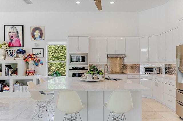 kitchen featuring backsplash, appliances with stainless steel finishes, a breakfast bar area, and white cabinetry