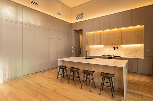 kitchen with a kitchen breakfast bar, sink, light hardwood / wood-style flooring, and an island with sink