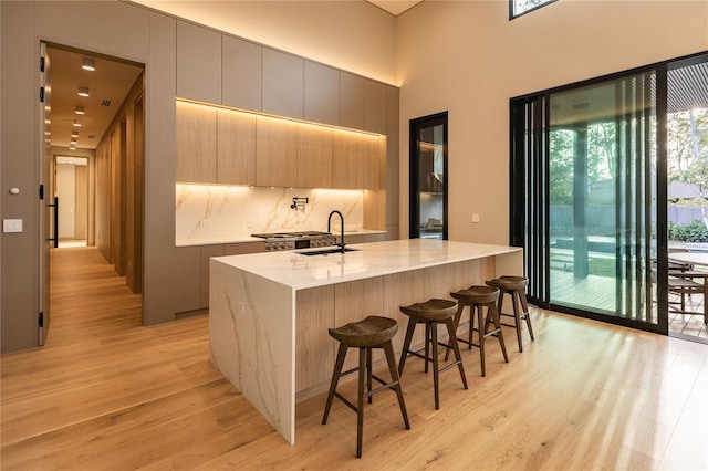 kitchen with a kitchen bar, sink, a kitchen island with sink, light wood-type flooring, and light stone counters