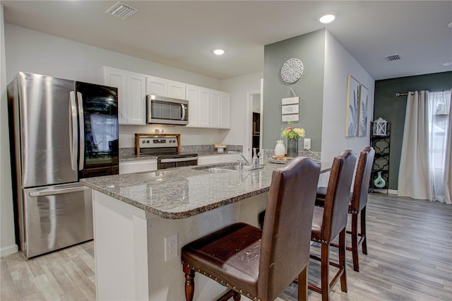 kitchen with sink, light stone counters, appliances with stainless steel finishes, light hardwood / wood-style floors, and white cabinets