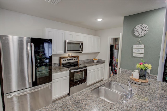 kitchen with stainless steel appliances, sink, white cabinets, and dark stone counters