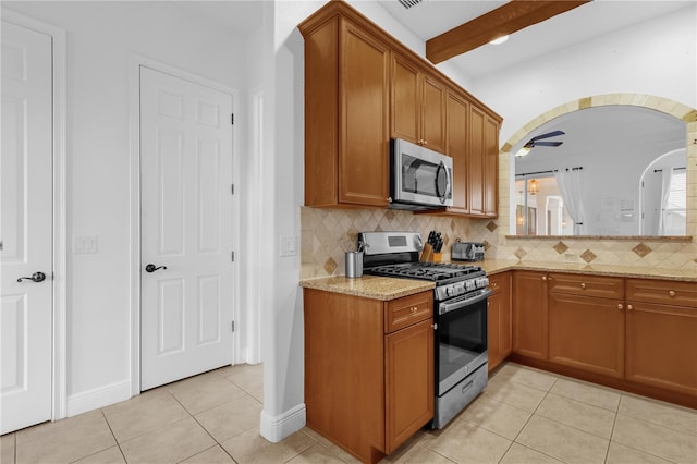 kitchen with light tile patterned flooring, beamed ceiling, ceiling fan, stainless steel appliances, and light stone countertops