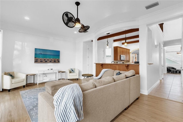 living room featuring ceiling fan, beam ceiling, and light wood-type flooring