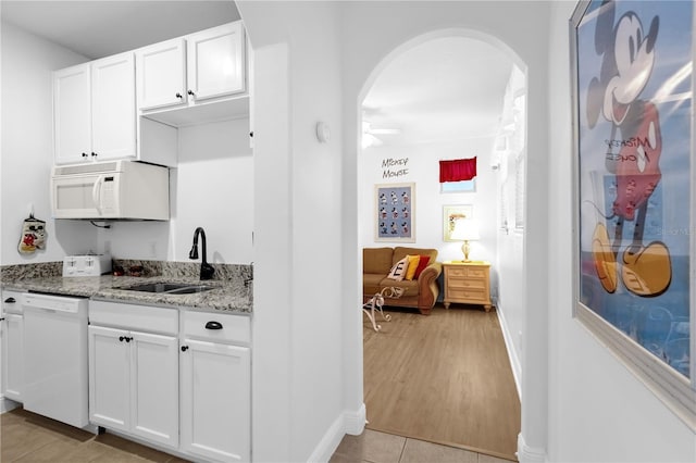 kitchen with white cabinetry, white appliances, light stone countertops, and sink