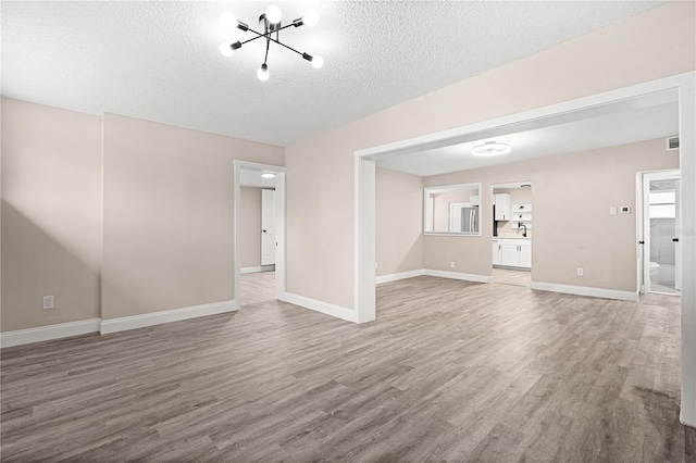 unfurnished living room featuring a notable chandelier, wood-type flooring, and a textured ceiling