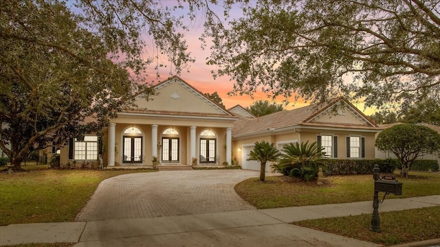 neoclassical home featuring a garage, a lawn, and french doors