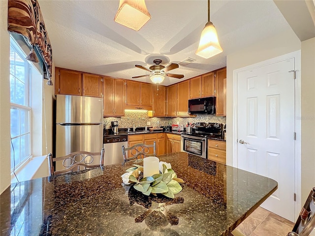 kitchen featuring tasteful backsplash, dark stone countertops, sink, hanging light fixtures, and stainless steel appliances