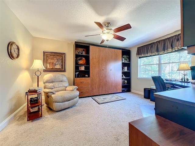 carpeted office space featuring ceiling fan, built in shelves, and a textured ceiling