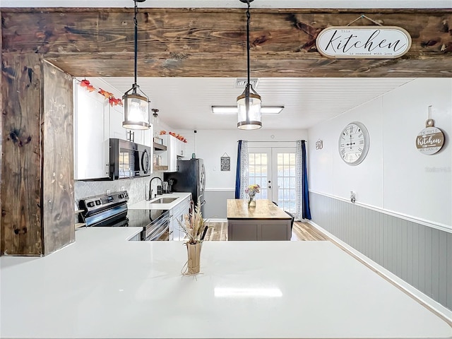 kitchen featuring sink, appliances with stainless steel finishes, kitchen peninsula, decorative light fixtures, and french doors