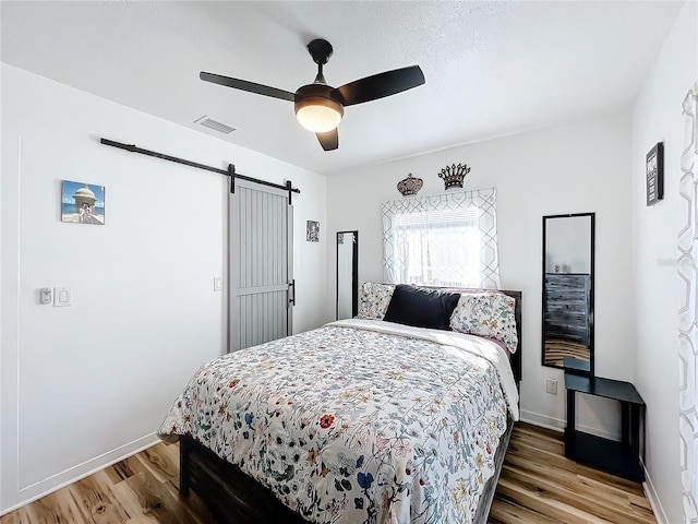 bedroom featuring hardwood / wood-style flooring, a barn door, and ceiling fan