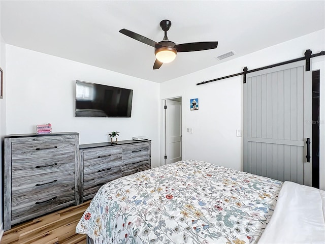 bedroom featuring ceiling fan, a barn door, and light wood-type flooring