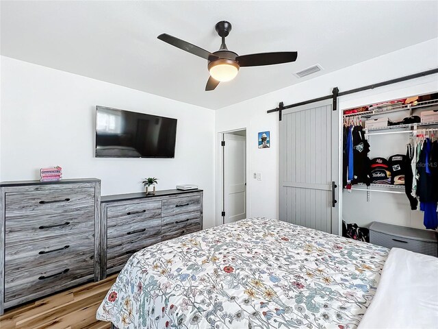 bedroom with a closet, light hardwood / wood-style floors, a barn door, and ceiling fan