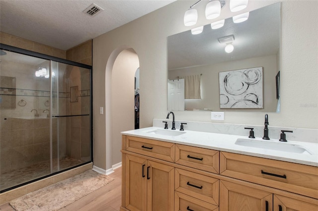 bathroom featuring wood-type flooring, a textured ceiling, an enclosed shower, and vanity