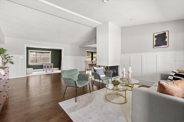 living area with a decorative wall, a brick fireplace, wood finished floors, lofted ceiling, and wainscoting