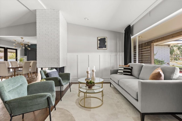 living room with vaulted ceiling, a chandelier, wainscoting, a decorative wall, and light wood-style floors