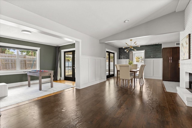 dining room featuring lofted ceiling, a chandelier, wood finished floors, wainscoting, and a brick fireplace
