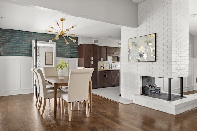 dining space with a chandelier, dark wood-type flooring, wainscoting, a decorative wall, and a fireplace