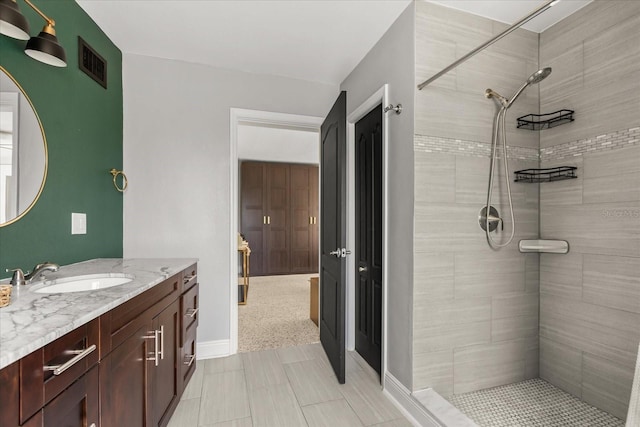 full bath featuring tiled shower, vanity, and baseboards