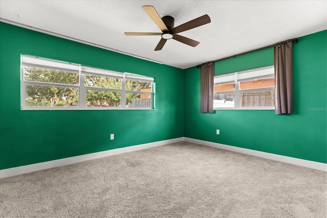 carpeted spare room with plenty of natural light, a ceiling fan, and baseboards