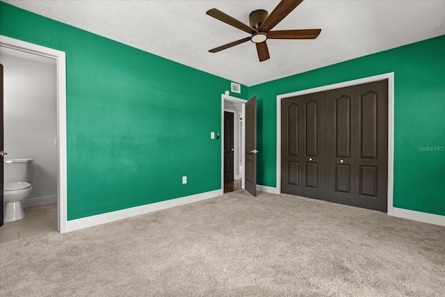 unfurnished bedroom with carpet floors, a closet, baseboards, ensuite bathroom, and ceiling fan