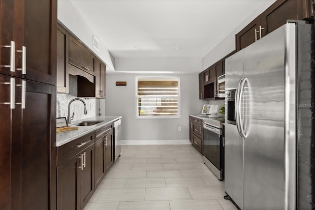 kitchen featuring stainless steel appliances, a sink, baseboards, and dark brown cabinetry