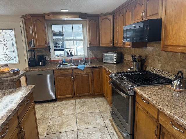 kitchen with backsplash, sink, stainless steel appliances, a textured ceiling, and light tile patterned floors