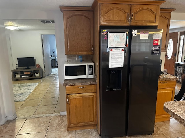 kitchen with black refrigerator with ice dispenser, light tile patterned flooring, and a textured ceiling